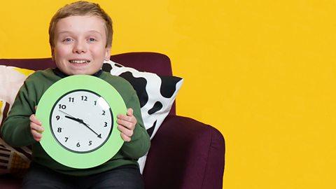 A person holding a clock and smiling on a sofa.