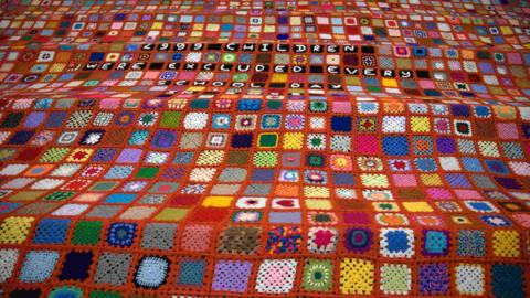 The red blanket, consisting of tiles in different colours and with the words 2,999 children were excluded every school day.