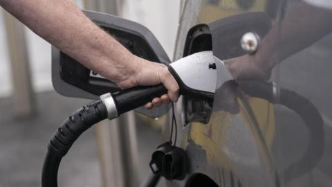 A person plugging an electric charger into a grey coloured car.