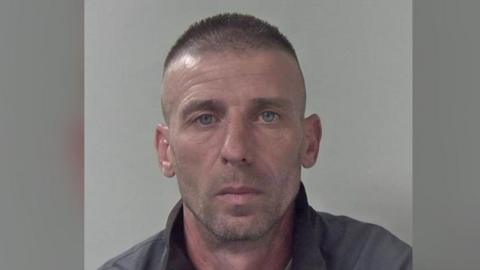 A police mugshot of Sorin-Costinel Ivan. He has grey hair and is wearing a grey fleece.