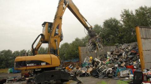 A yellow crane next to a pile of rubbish. 