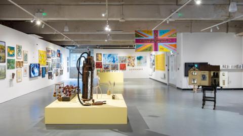 A gallery with a variety of artworks on display against white walls and a grey floor