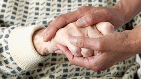 A person, patting someone's hands, a stock image, showing a person wearing a black and cream jumper.