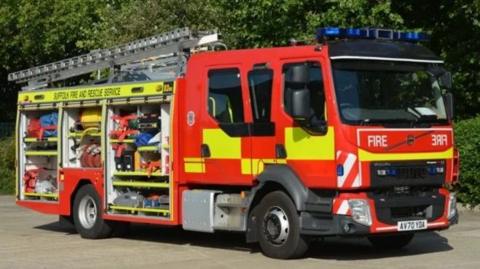 A Suffolk Fire and Rescue Service engine seen from the side with its side panels open, showing rolled up hoses and other firefighting equipment