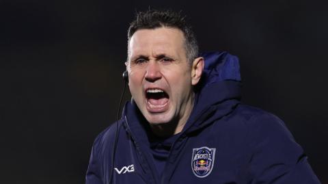 Stephen Jones, with an earpiece in his right ear and wearing a big branded navy Newcastle Red Bulls jacket, shouting instructions at his players