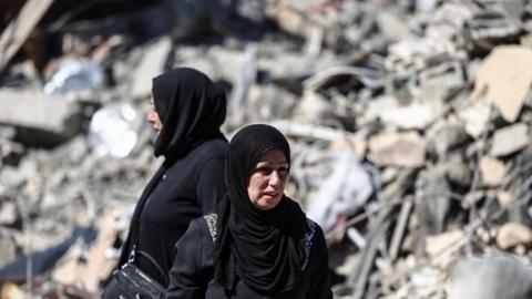 Women stand at the site of an Israeli strike near the Rafik Hariri University Hospital,