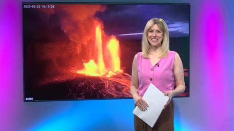 Jenny in the studio with an erupting volcano in the screen