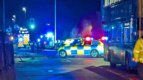 Emergency services with blue lights in dark at scene of a crash.