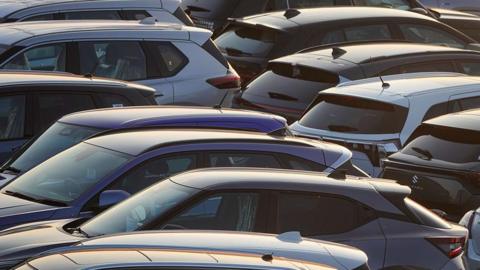 About ten cars are packed into a small space outside after being imported, ready to go to their new homes - they look to be shiny and in good condition.