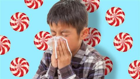 A boy blowing his nose in front of a blue background with peppermints behind him. 