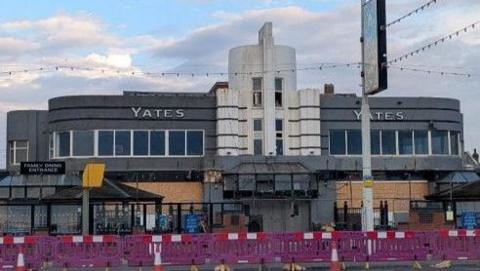 Google streetview of the grey and white Art Deco building with purple barriers set up in front.