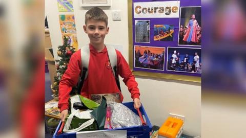 A schoolboy holding a box of toys