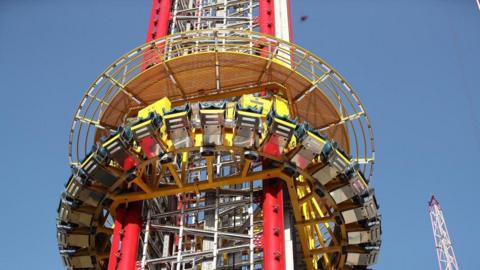 A tall theme park drop ride, with seats circling a central pillar 