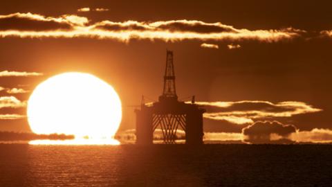 The sun behind an oil rig in the North Sea. The photo is an orange colour because of the light.