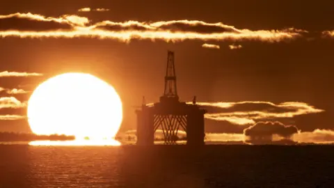 The sun behind an oil rig in the North Sea. The photo is an orange colour because of the light.
