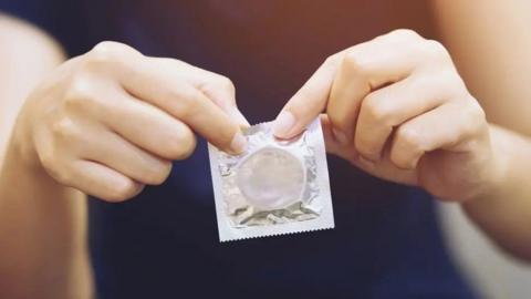 Close up of hands holding a condom. 
