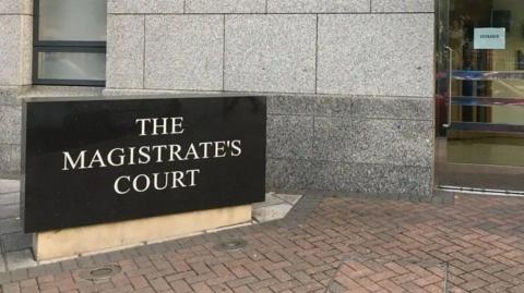 A stone sign which reads THE MAGISTRATE'S COURT. There is a glass door leading in to the building to the right.