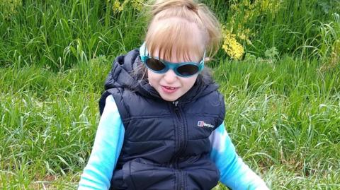 Jaydi wearing a dark blue gillet over a light blue fleece with her hair tied up in a pony tail and wearing a pair of sunglassess.