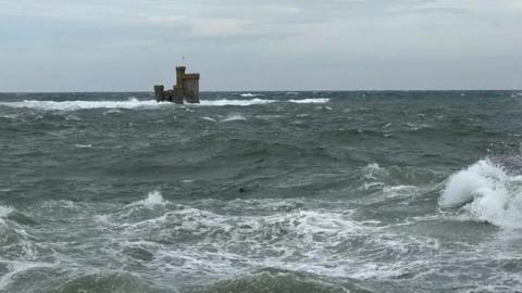 The tower of refuge, which is a small castle-like building in Douglas Bay, surrounded by rough seas.