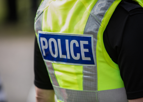 The back of a high-vis jacket with the word "police" across it. The jacket is green/yellow and the sleeves are black