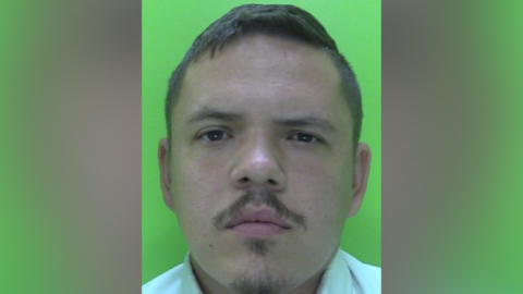 A police mugshot of a man with a goatee beard and moustache