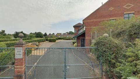 Gates pictured at the entrance of a large brick building. Bushes can be seen in the background.