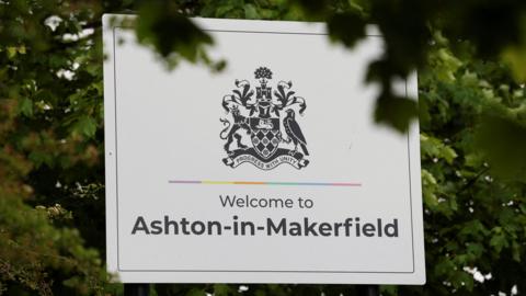 A large black and white "Welcome to Ashton-in-Makerfield" roadsign