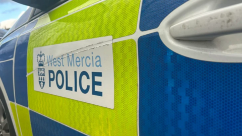 The side of a white police car with yellow and blue squares on the side.