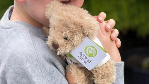 Child holding a little light brown teddy beard