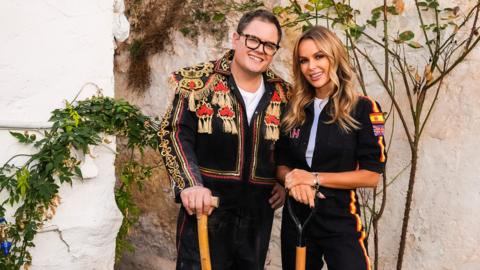 Alan Carr and Amanda Holden in bullfighting costumes in front of a Spanish house