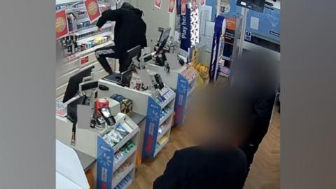 A man dressed in black climbing over a supermarket counter