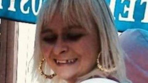 Melissa Eastick smiling and looking down. She has blonde hair, large hooped earrings and blue eye shadow