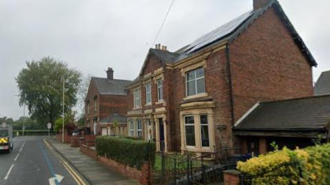 A Google Streetview screenshot of Surrey Street in Jarrow. It is a residential street with two large properties in red brick. The street has double yellow lines outside the properties.