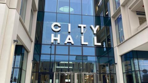 The entrance of Sunderland City Council headquarters. The sign above the glass fronted building reads "city hall".
