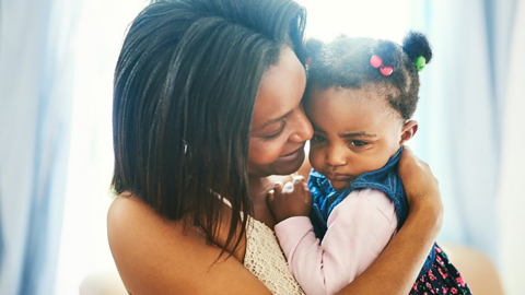 Young girl looks upset, while being cradled by her mum.