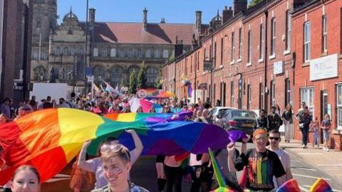 Those walking the parade carry a rainbow flag through a Wakefield street.