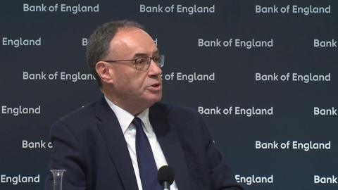 Bank of England governor Andrew Bailey speaking at a news conference. He is wearing a dark blue suit, white shirt and dark blue tie, and sitting in front of a screen with 'Bank of England' written on it