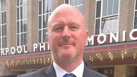 David Ellis poses in a suit and tie outside the Liverpool Philharmonic hall entrance.