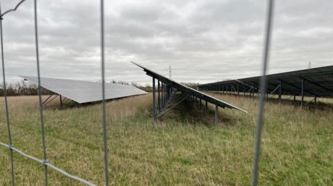 North Angle Solar Farm panels in a field, behind a wired fence.