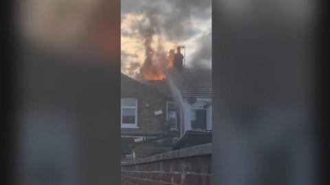 A house fire, with the roof ablaze, is being tackled by fire fighters 