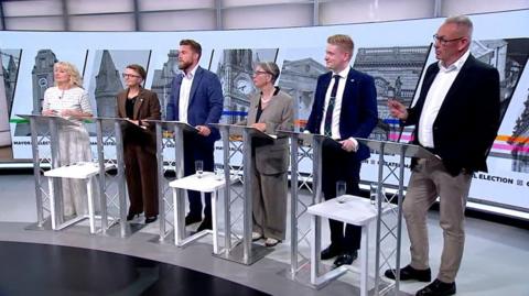 The candidates for Greater Manchester mayor stand behind lecterns in a TV studio