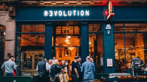 A Revolution branded bar with revellers gathered outside.