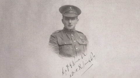 WW1 photo of Frederick Room in his army uniform, fully buttoned up. He is wearing a standard-issue peaked cap, synonymous with WW1 soldiers. His name is written in scrawled pencil below the photo.