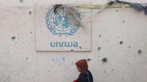 A Palestinian woman walks past a damaged wall bearing the Unrwa logo at a camp for internally displaced people in Rafah, southern Gaza Strip, on 28 May 2024