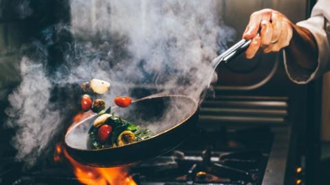 A stock image of a chef frying vegetables in a wok.