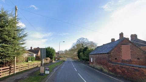 Streetview image of Church Lane, Horsley Woodhouse, a rural village road with residential houses on one side and farm buildings on the other