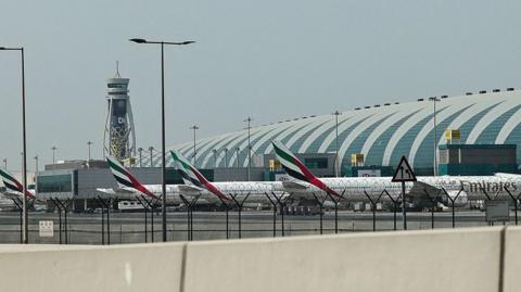 Three Emirates planes lined up at Dubai International Airport, a control tower stands in the background.