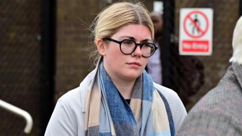 Ciara Corvan, with tied up blonde hair, wearing glasses, a blue and beige scarf and a grey jacket. 