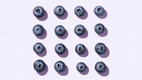 Blueberries arranged in a square on a light purple background