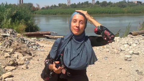 An undated image of Shelly Kittleson. She wears a hijab and holds a phone while standing in front of a river